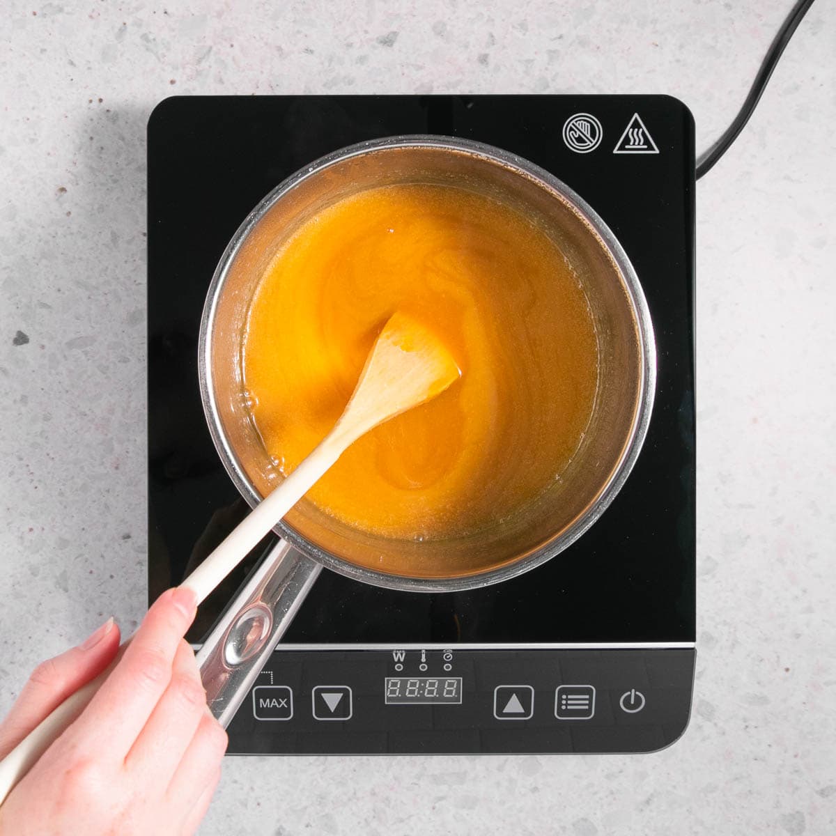 The caramel sauce being stirred with a long handled wooden spoon.