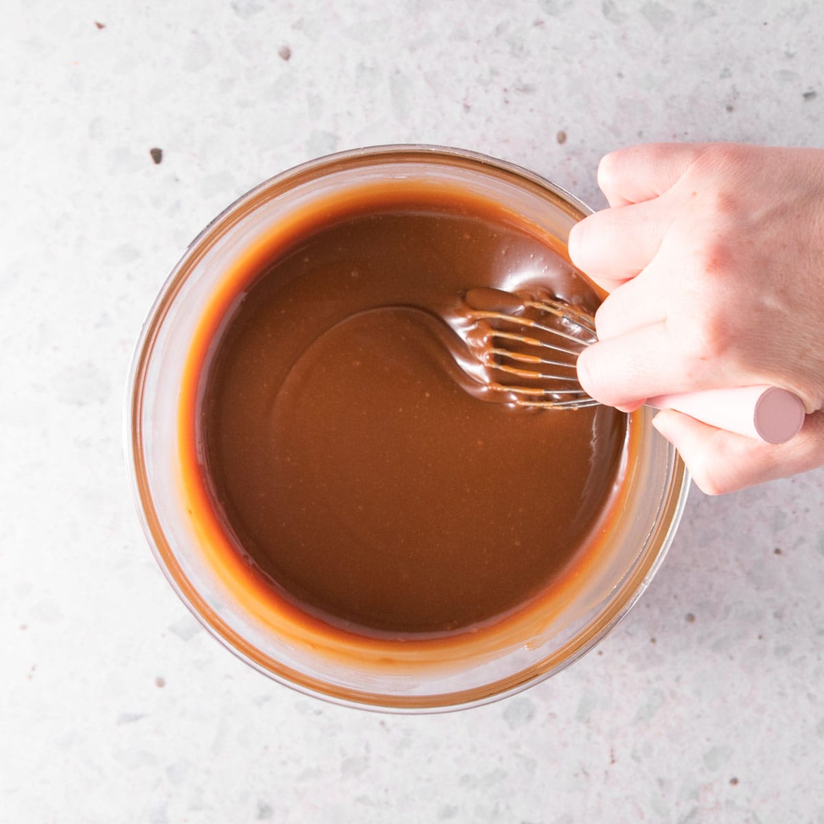 A hand stirring the finished sauce with a pink-handled whisk.