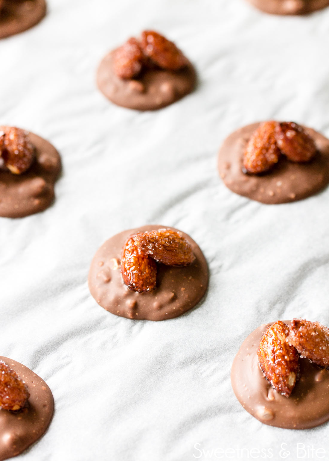 Small blobs of melted Toblerone on baking paper, each topped with two honey roasted almonds.