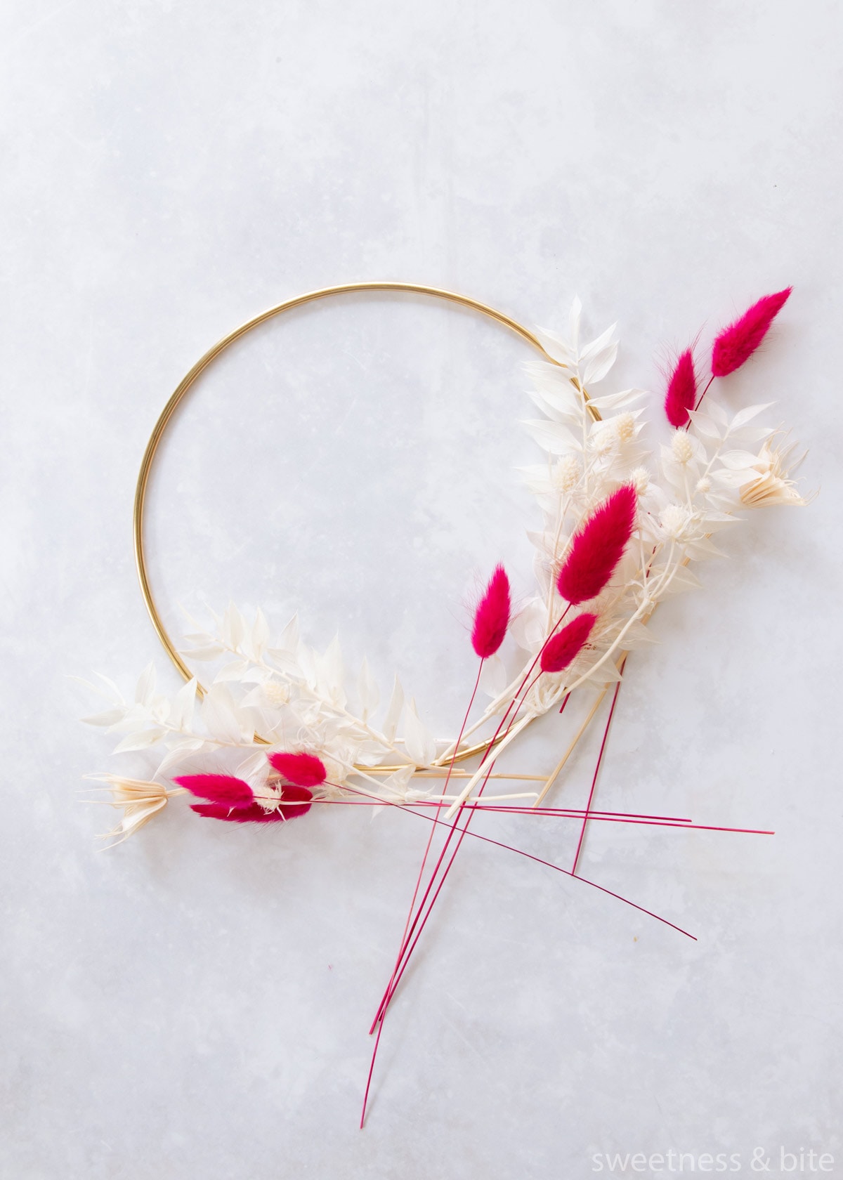 A gold hoop with white and pink preserved flowers and foliage arranged in a rough design.