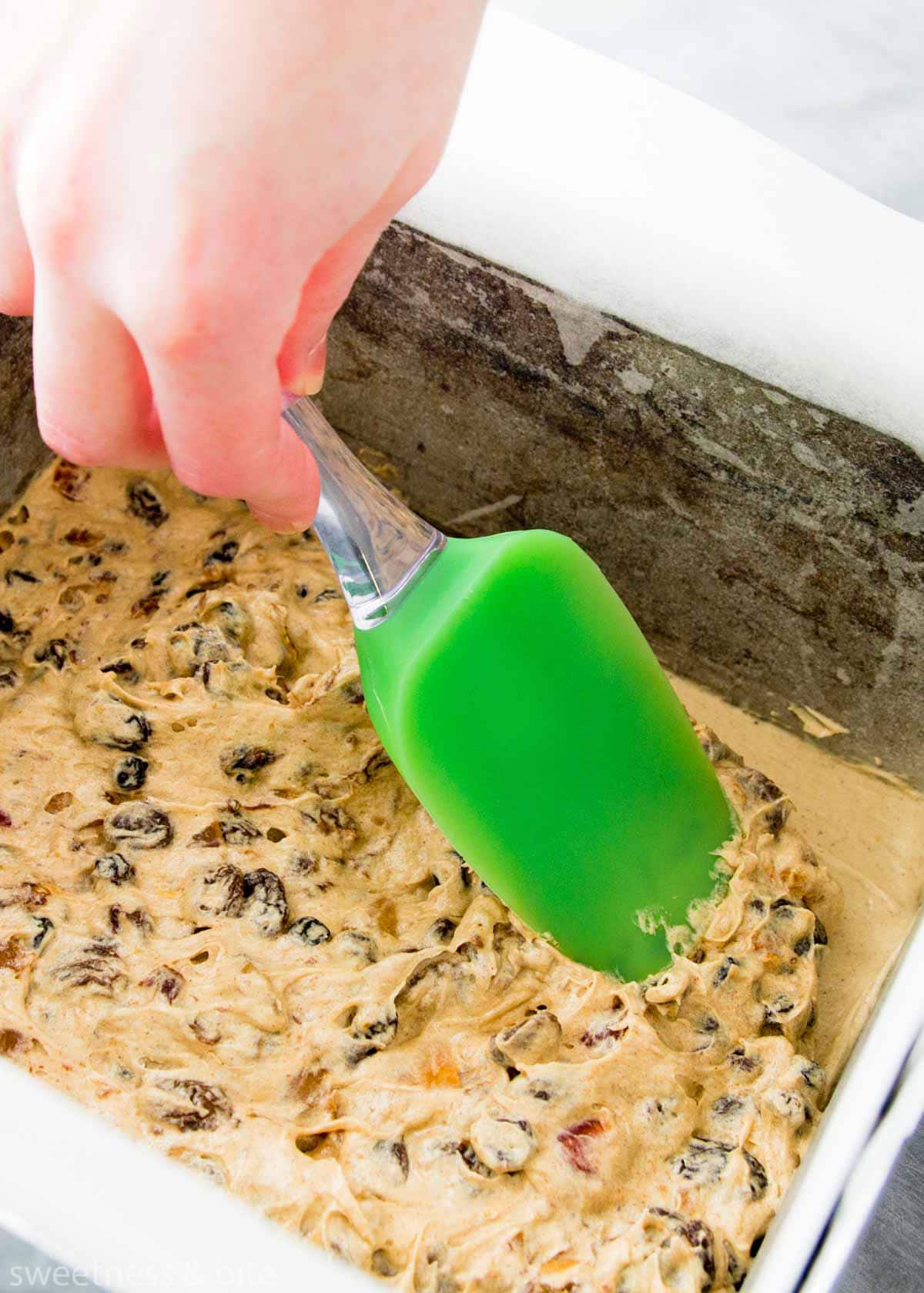 Christmas cake batter being pressed into the prepared cake pan with the back of a spatula.