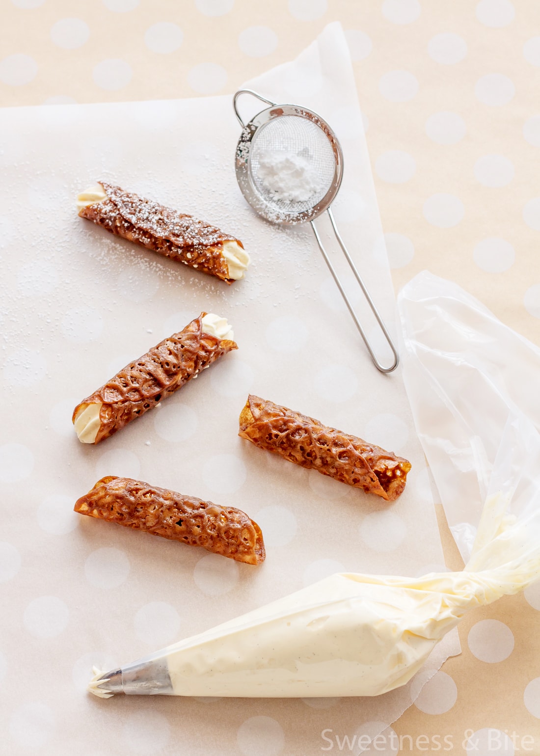 Four brandy snaps on a piece of baking paper, with a small sieve holding icing sugar.