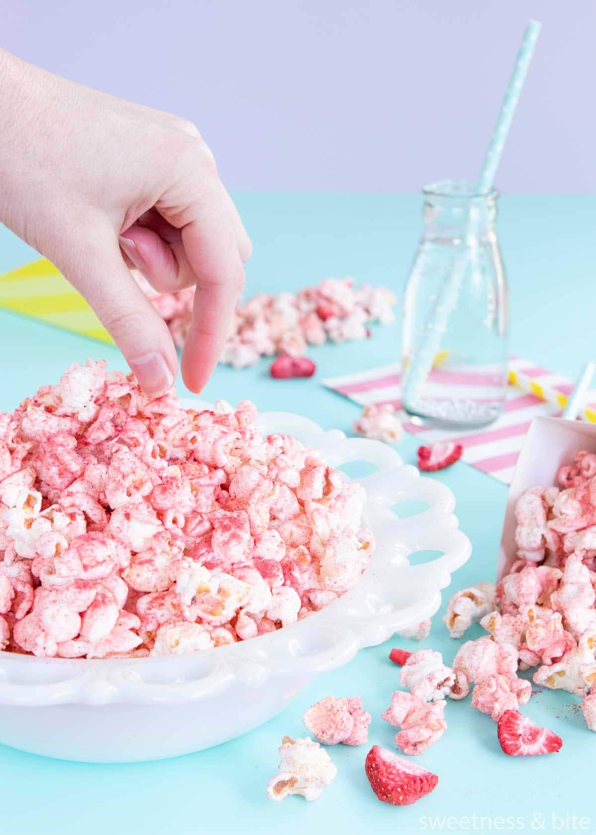 A hand about to pick up some fruity popcorn from a white bowl.