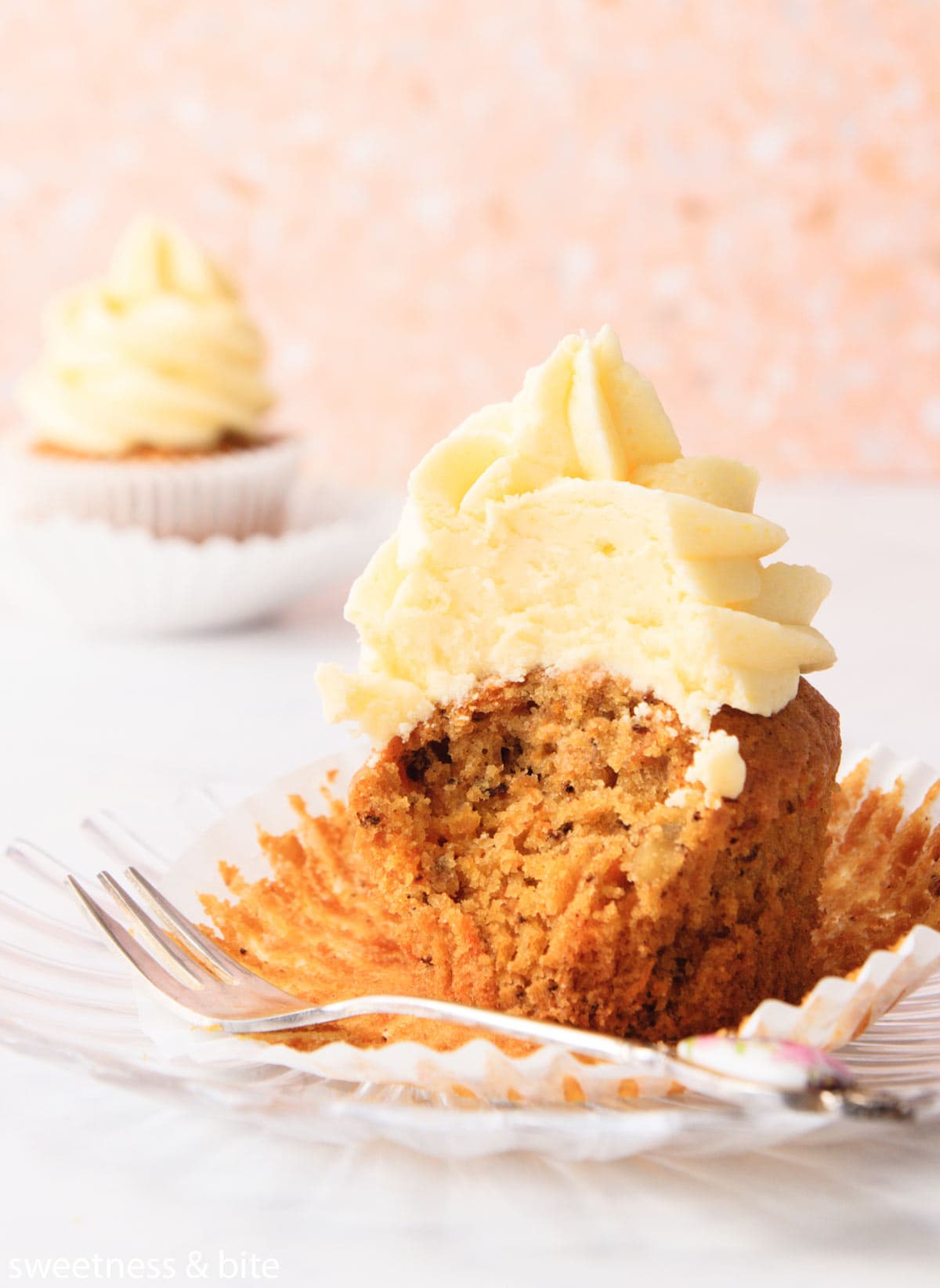 A carrot cupcake with a bite taken out of it, sitting on the peeled cupcake liner.