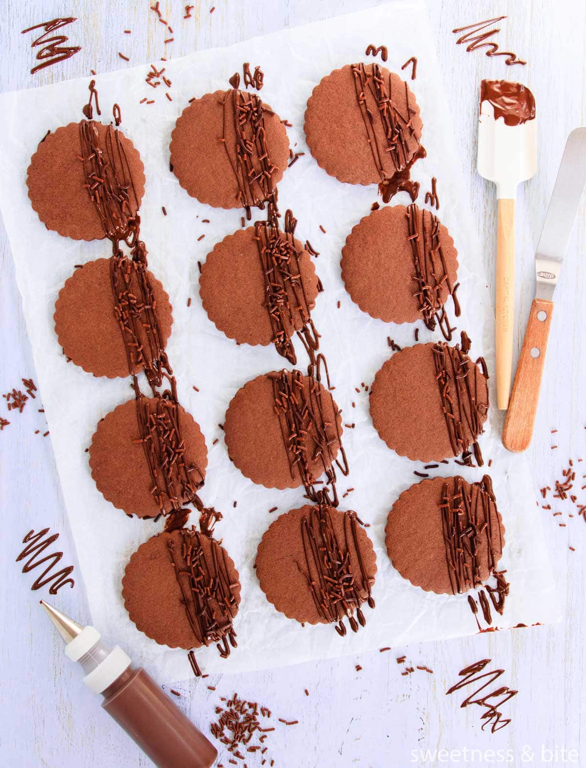 Chocolate cookies, drizzled with melted dark chocolate, with chocolate sprinkles, on a blue woodgrain background.