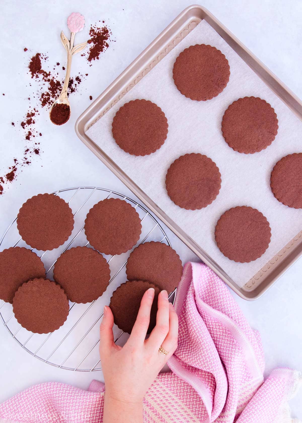 Cookies on a baking tray and arranged on a round cooling rack, with a hand taking a cookie.