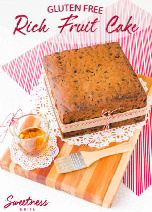 A gluten free fruit cake sitting on a wooden board, with a red and white striped cloth underneath.