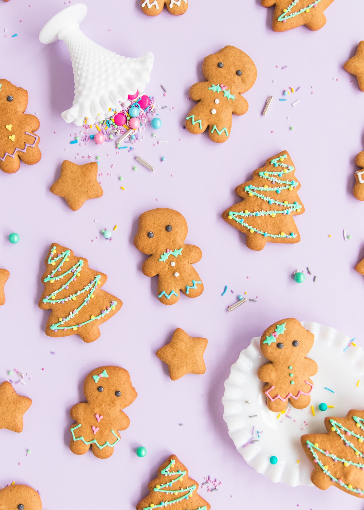 Gluten free gingerbread men and women with gingerbread Christmas tree and star cookies on a purple background, surrounded by pastel and metallic sprinkles.