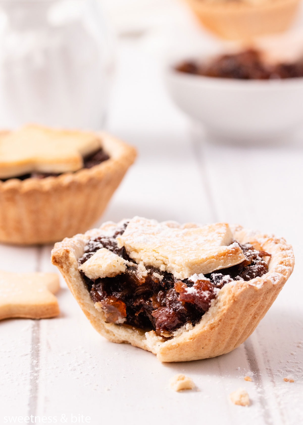 Close up of a bitten gluten free mince pie, showing the crisp base and sticky mincemeat filling.