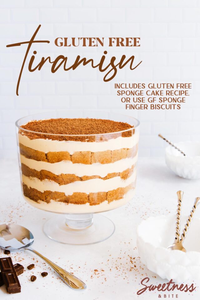 Gluten free tiramisu in a footed glass trifle bowl, on a grey/blue background, with small white bowls and a serving spoon.