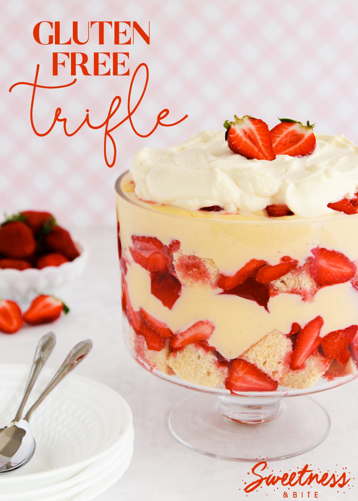 Gluten free trifle in a footed glass bowl on a pink background.