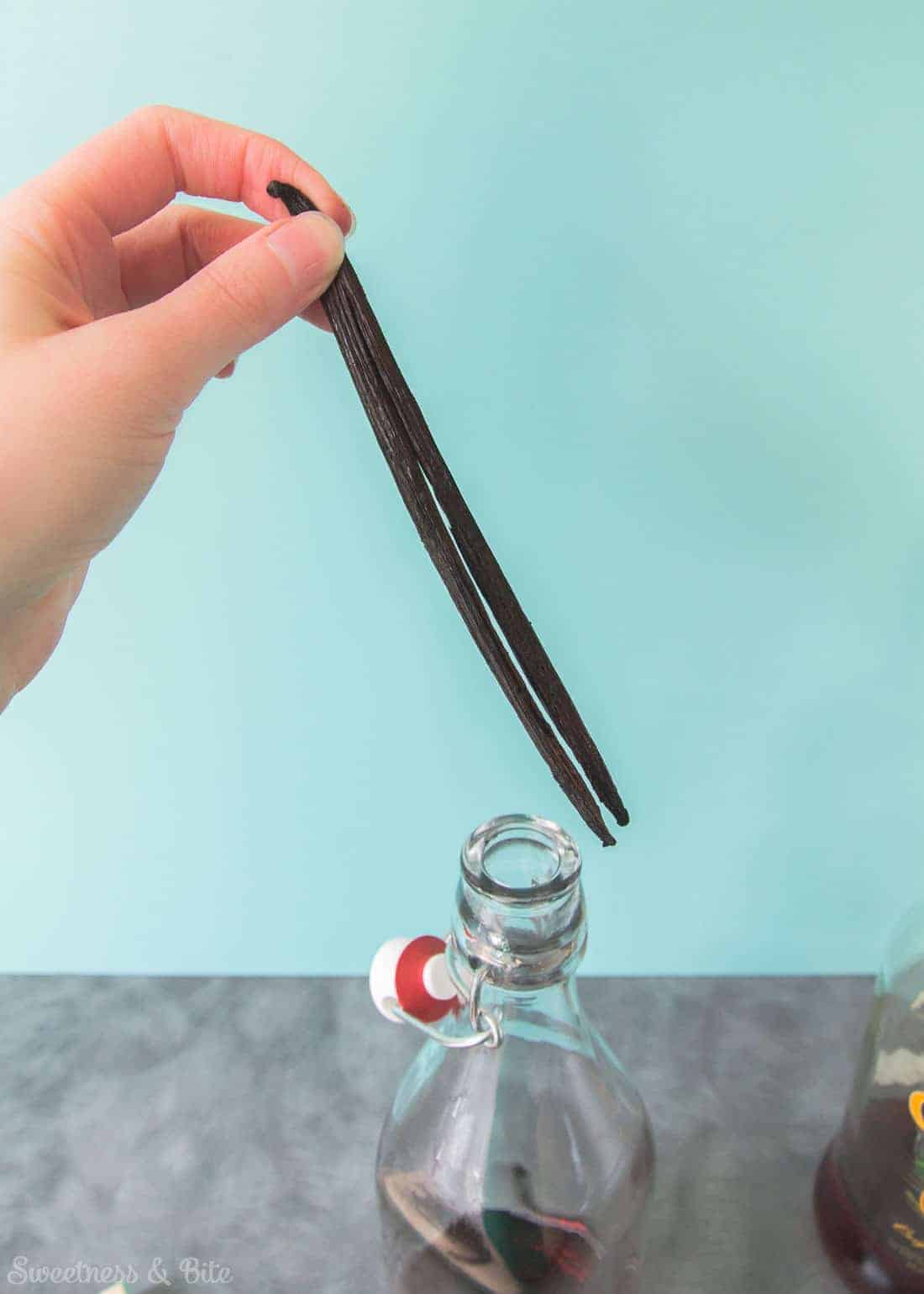 A vanilla bean being put into the bottle, split end down.