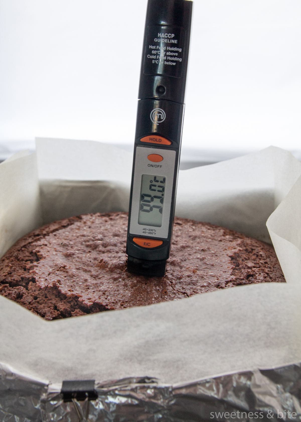 A probe thermometer inserted into a chocolate cake showing the internal temperature is 99 degrees Celcius.