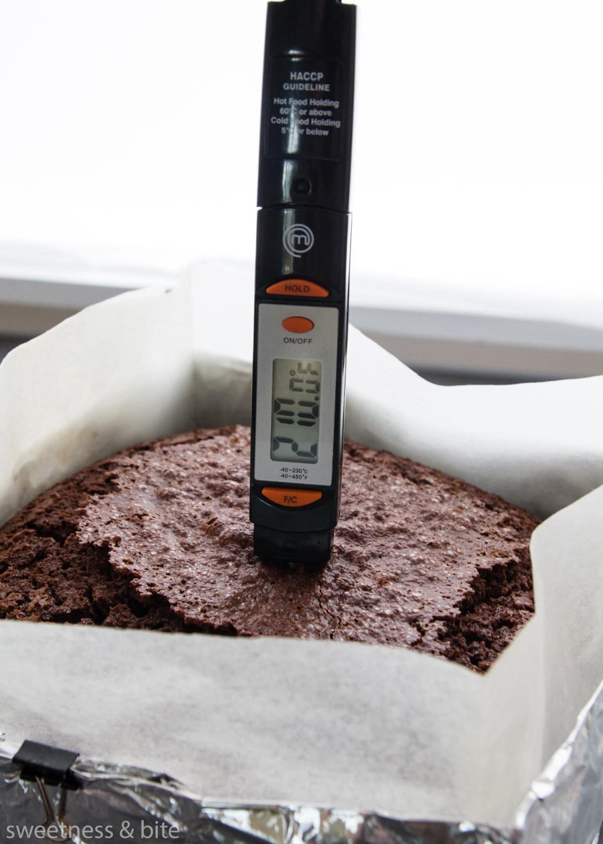 A probe thermometer inserted into a chocolate cake showing the internal temperature is 210 degrees Fahrenheit.