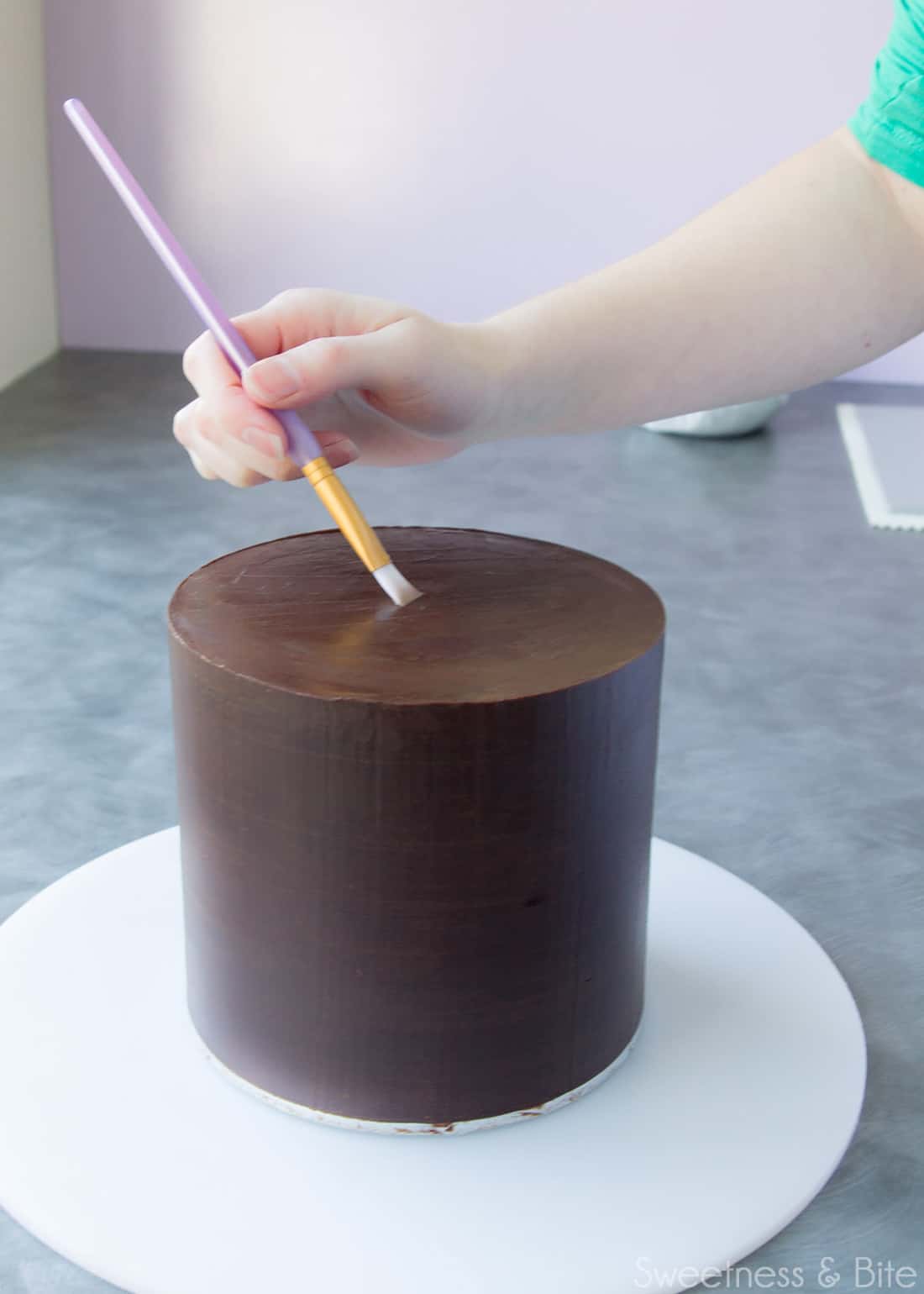 Painting vodka onto the top of a chocolate ganache covered cake.