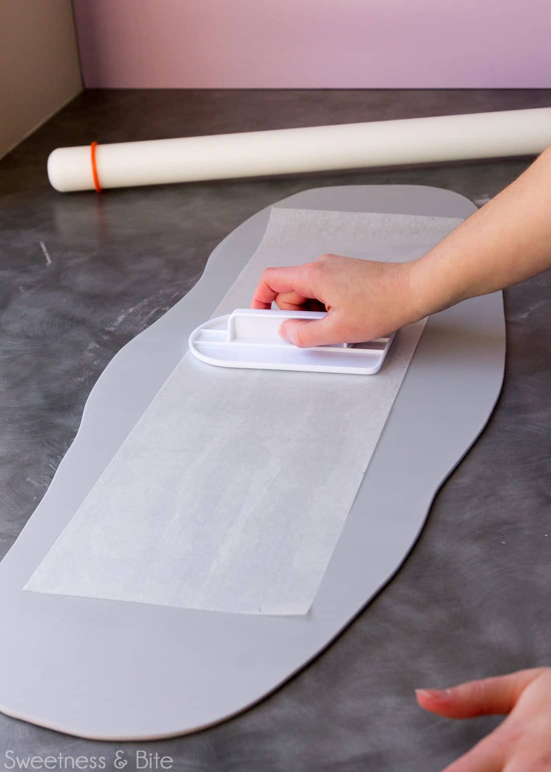 A hand using a fondant smoother to press the template onto the rolled out fondant.