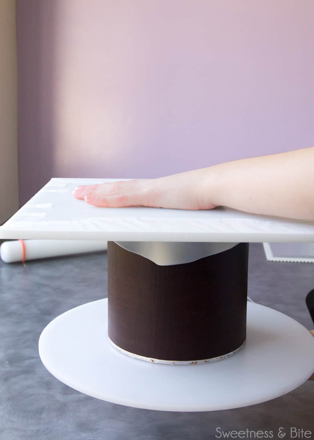 The waxed paper covered board being placed on top of the cake.