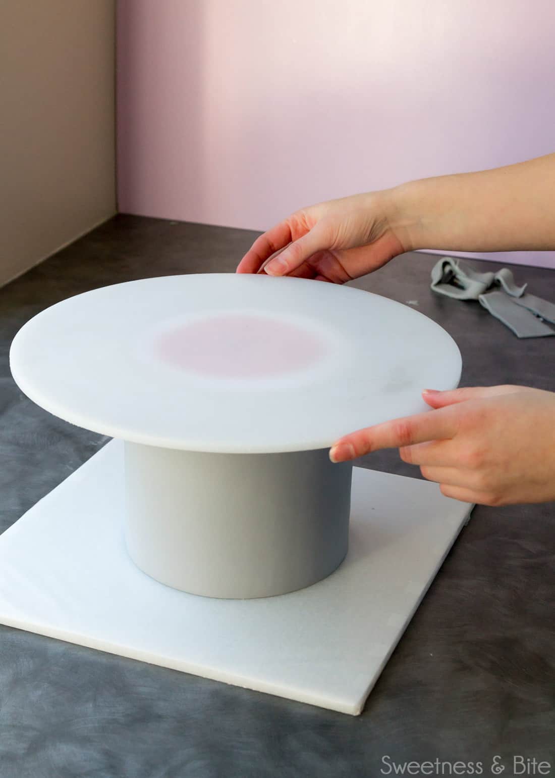 A large round acrylic cake board being placed onto the cake. 