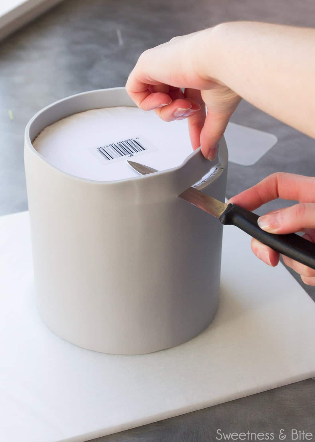 A knife being used to trim the excess fondant from the top of the cake.