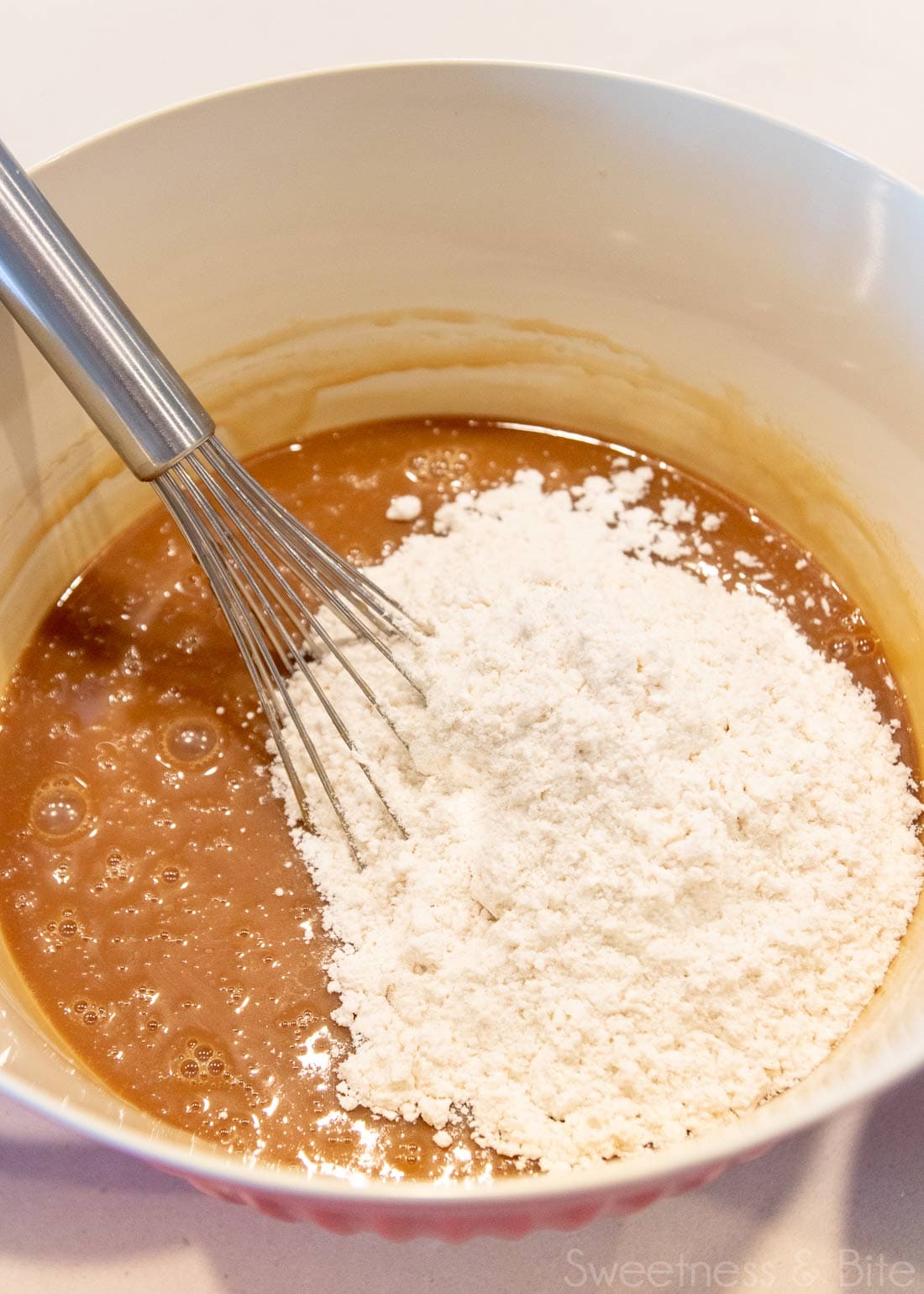 Large bowl with caramel mud cake batter and a balloon whisk. 