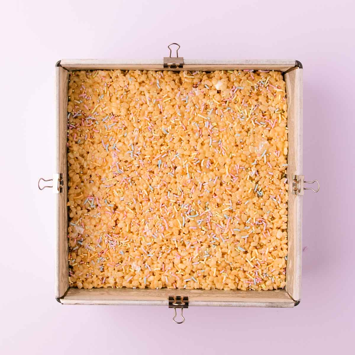 The mixture pressed into an even layer in the square pan, and sprinkled with pastel sprinkles.