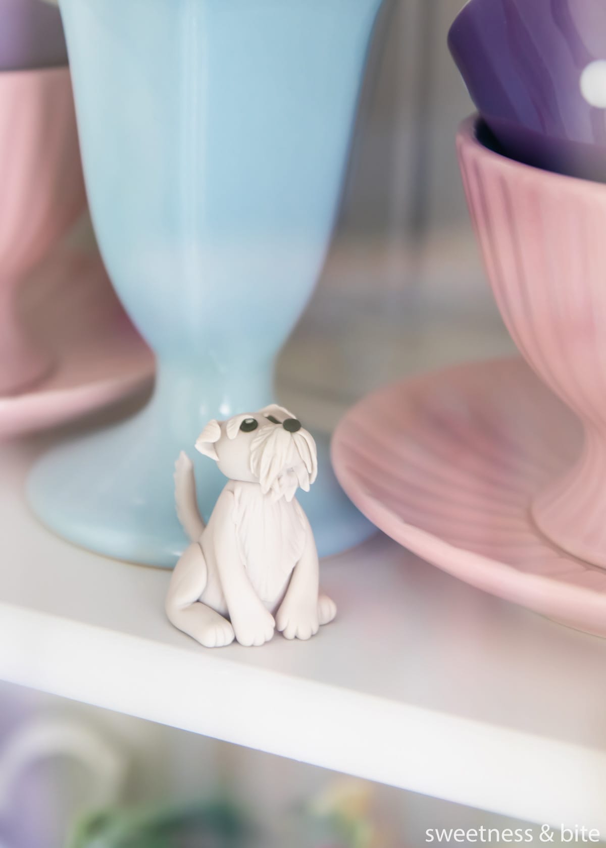 A small grey dog gumpaste cake topper being stored in a glass-door cabinet.