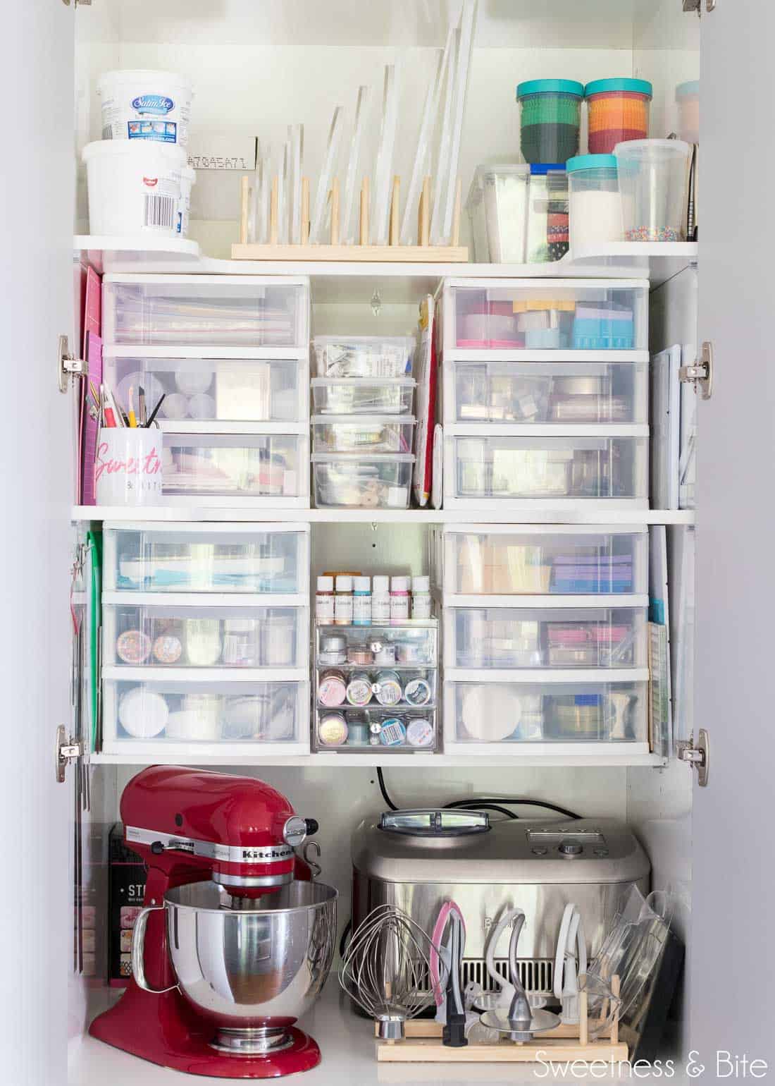 Close up of the upper shelves of the cake pantry, with plastic drawers filled with tools, and a red Kitchen-Aid stand mixer.