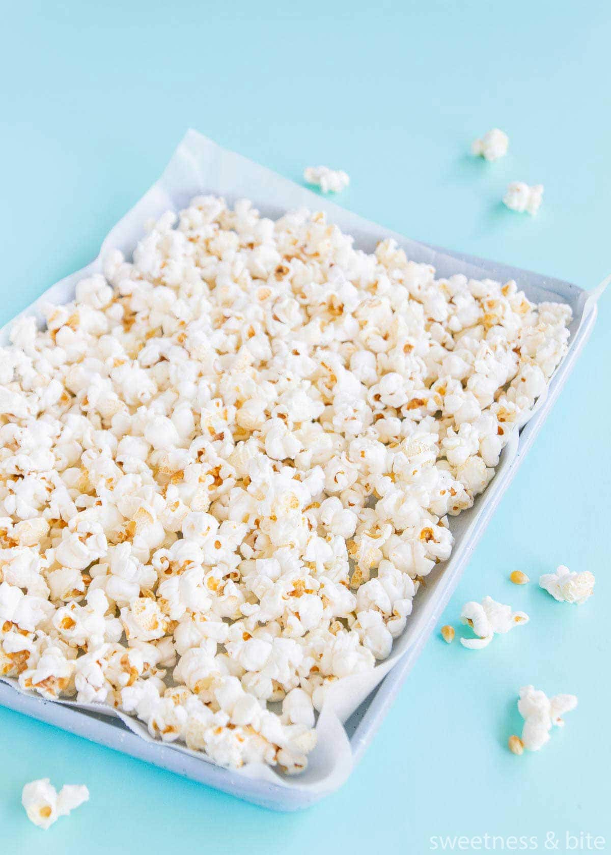 A tray of plain, popped popcorn on a blue background.